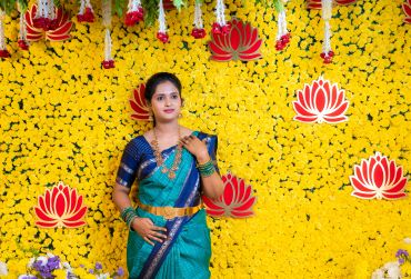 Woman in traditional attire posing against a yellow flower backdrop.