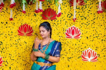 Woman in traditional attire stands against a yellow flower backdrop with floral decorations.
