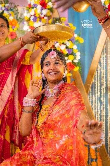 Smiling woman in traditional attire enjoys ritual with flower jewelry and turmeric.