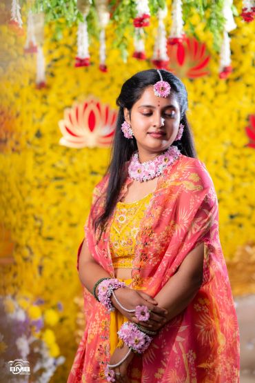 Woman in traditional attire with floral jewelry posing against a yellow floral backdrop.