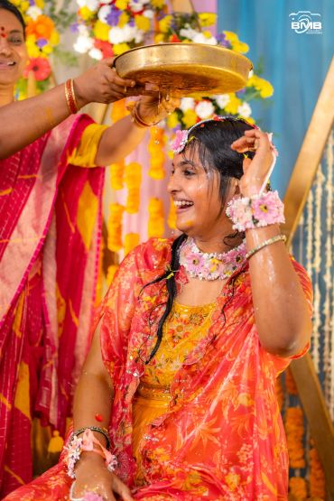 Woman smiling during a traditional ceremony with flowers and colorful attire.