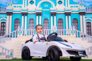 A toddler driving a toy car in front of a grand building.