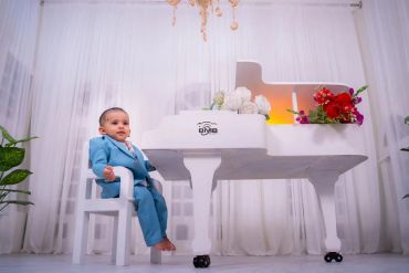Toddler in blue suit sitting beside a white piano.