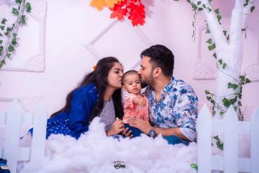 Parents kissing their baby in a dreamy setting.