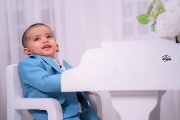 Toddler in a blue suit sitting at a white piano.