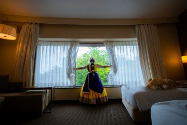 Woman in traditional dress opening curtains to a garden view.