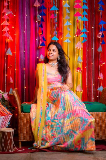 Woman in vibrant traditional dress smiles amid colorful decorations.