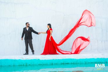 Couple posing with flowing red dress against a white background.