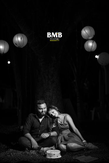 Couple sitting closely with a cake in front, under hanging lanterns.