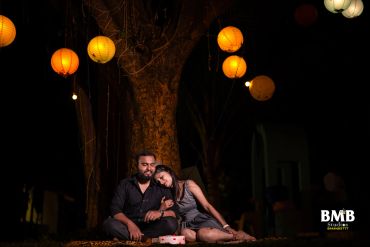 Couple celebrating with cake under lantern-lit tree at night.
