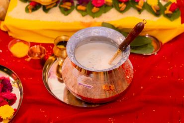 Traditional copper pot with white liquid and ritual items on red cloth.