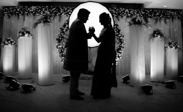 Silhouetted couple holding hands against wedding-themed backdrop.