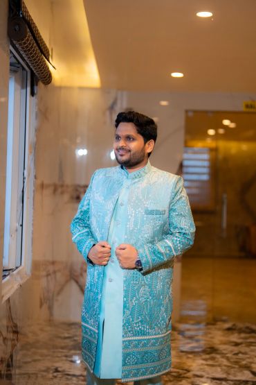 Man in traditional light blue embroidered attire looking out a window.