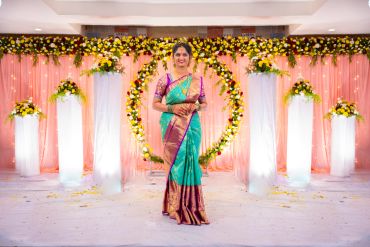Woman in traditional saree standing in decorated venue.