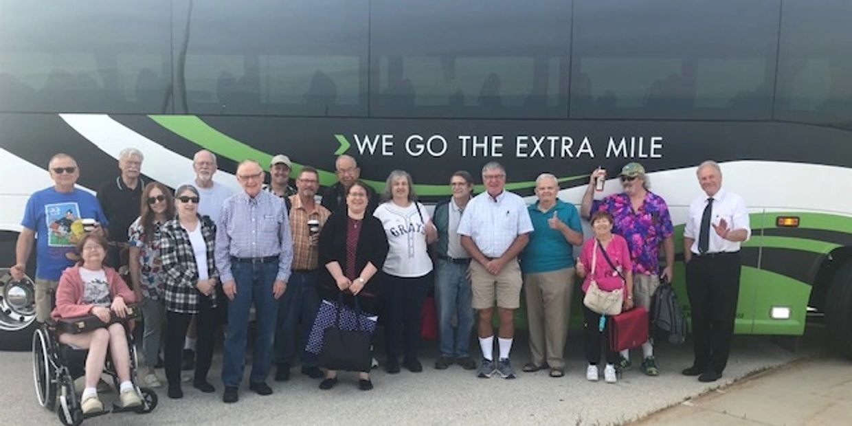 Group of people posing in front of a bus with 'We Go The Extra Mile' slogan.