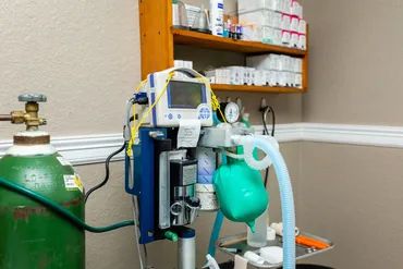 Medical ventilator setup with oxygen tank in a clinical room.