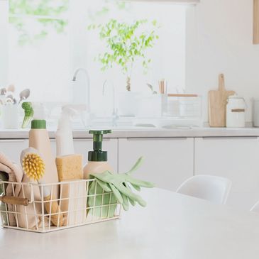 Basket of cleaning supplies in a bright kitchen.