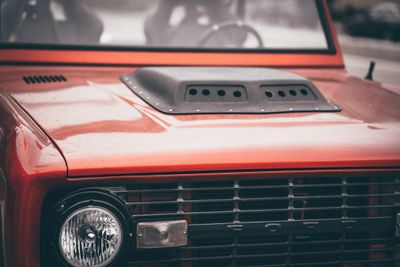 Close-up of a vintage red car's front grille and headlight.