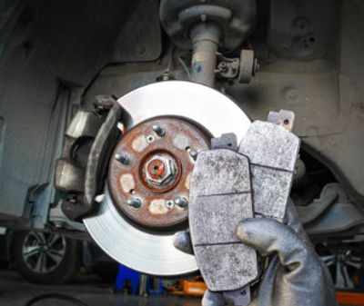Worn brake pads held near a car's brake disc.