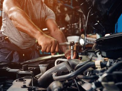 Mechanic tightening a bolt under a car hood with a wrench.