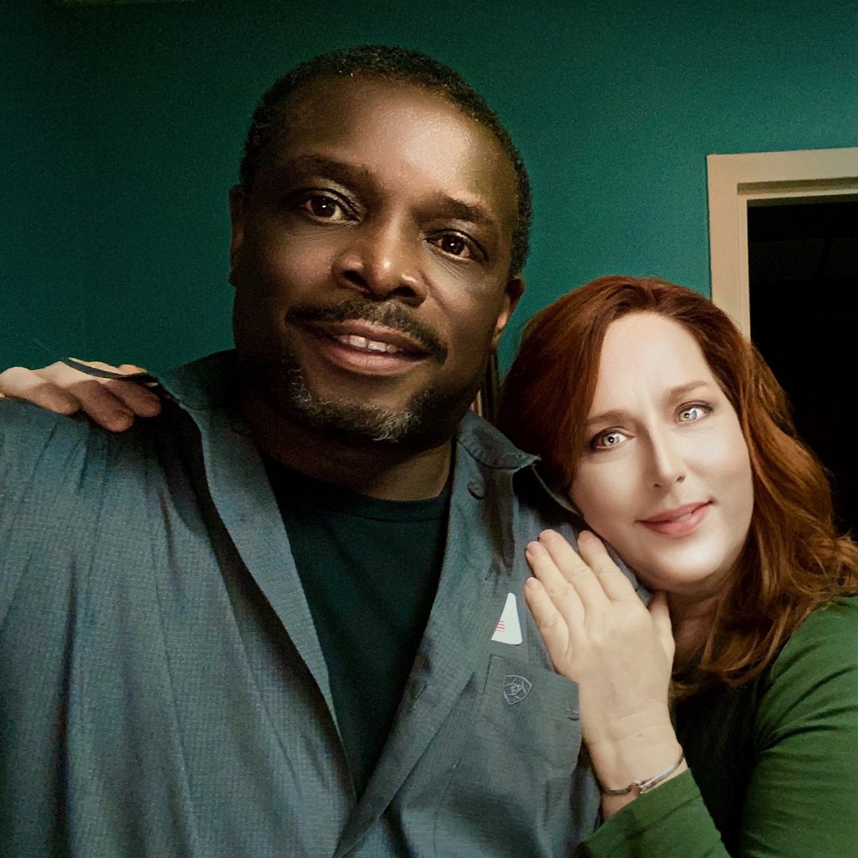Smiling couple posing closely indoors with a teal wall background.