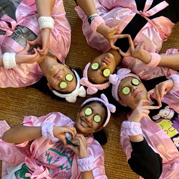 Four friends in pink robes and cucumber masks having fun.