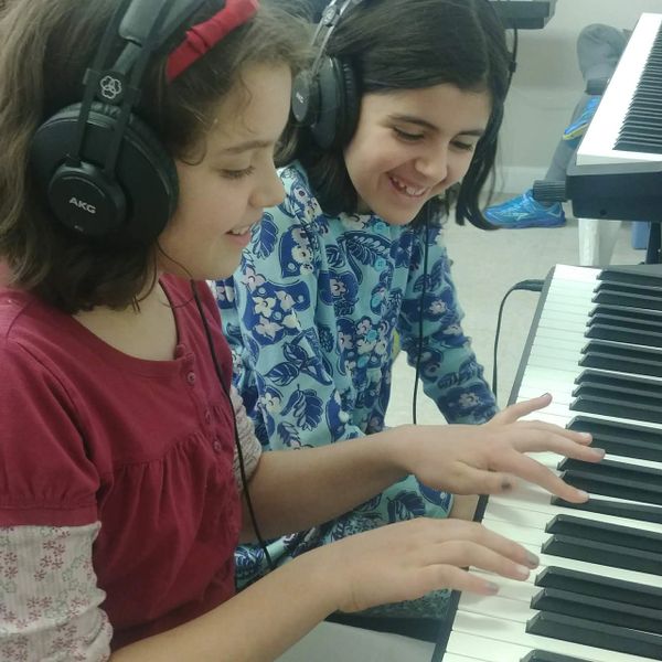 Two smiling girls playing piano together on headphones