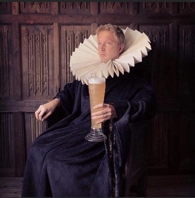 Person in historical attire with a large ruffled collar holding a tall glass of beer.