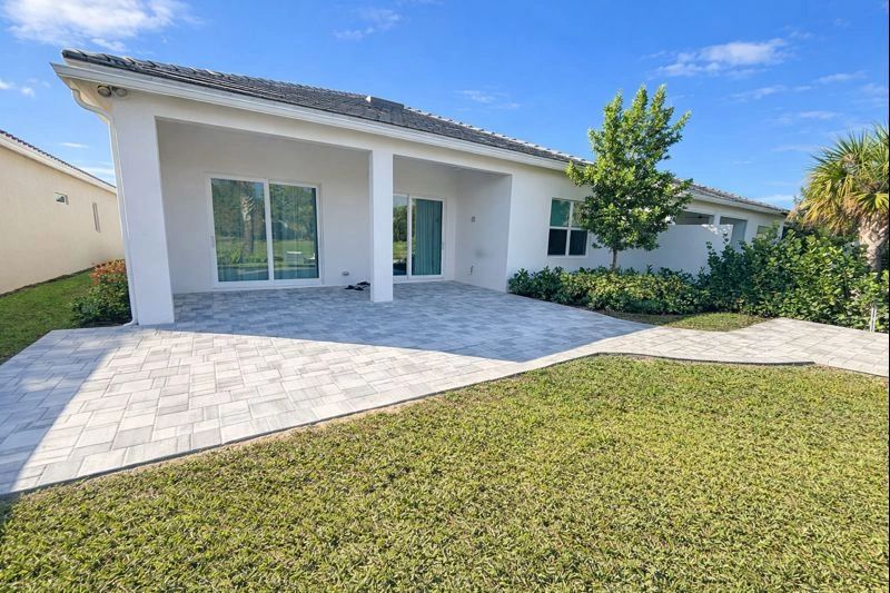 Modern white house with spacious tiled patio and green lawn under blue sky.