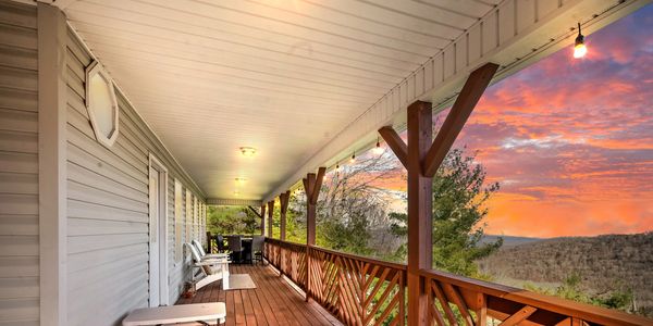 A wooden porch with chairs and a picnic table overlooking a scenic sunset.