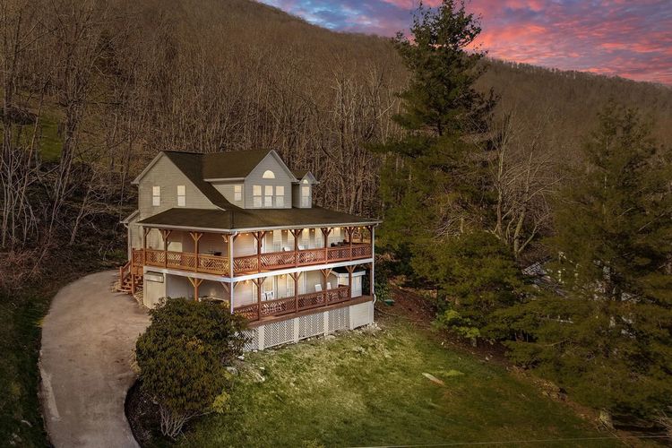 A cozy two-story house with wooden balconies nestled against a wooded hillside at sunset.