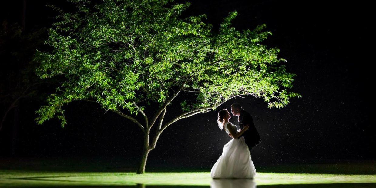 Couple dancing under a tree at night with rain.