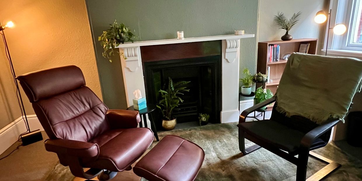Cozy sitting area with leather armchair and ottoman by a fireplace.