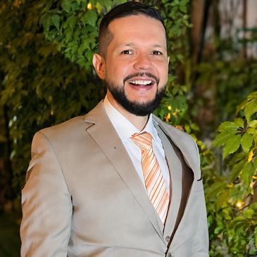 Hombre sonriente con traje beige y corbata naranja.
