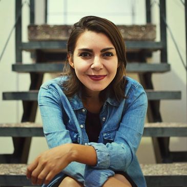 Young woman smiling while sitting on stairs, wearing a denim jacket.