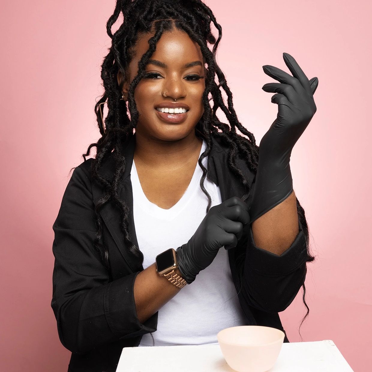 Bri the Esthi professional headshot posing with facial implements and gloves against pink background
