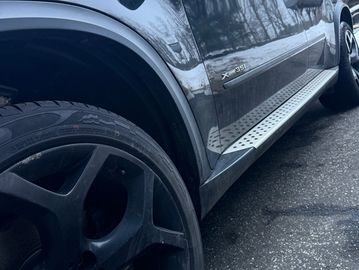Close-up of a black BMW X5 with black rims on a wet road.