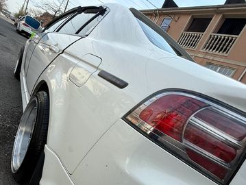 Close-up of a white car's rear side with custom rims and tinted windows.