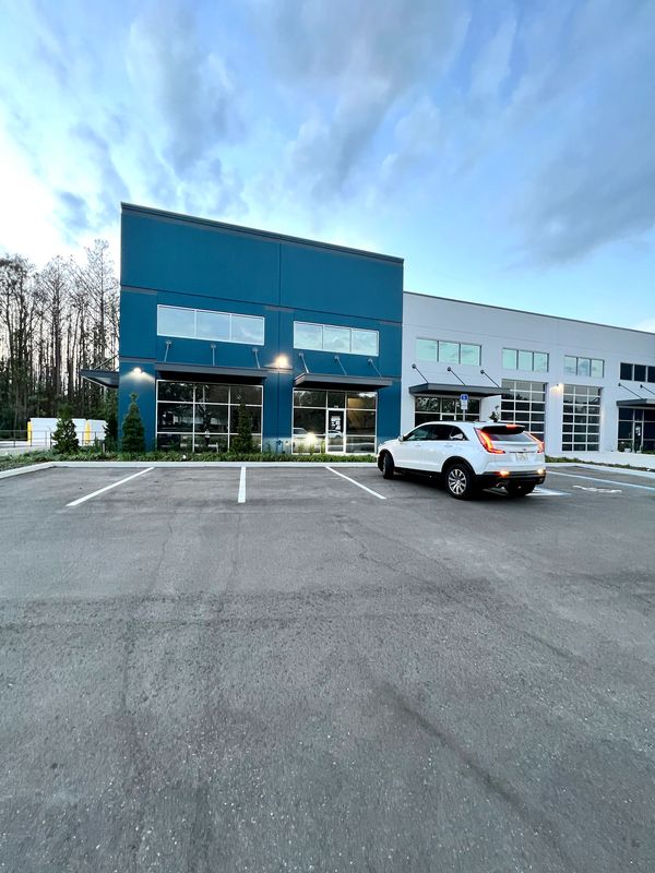 Empty parking lot with one white car near a blue and white commercial building.