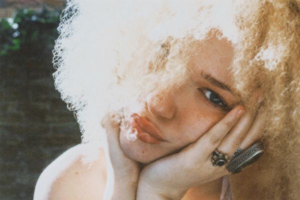 Pensive woman with curly blonde hair resting her face on her hands.