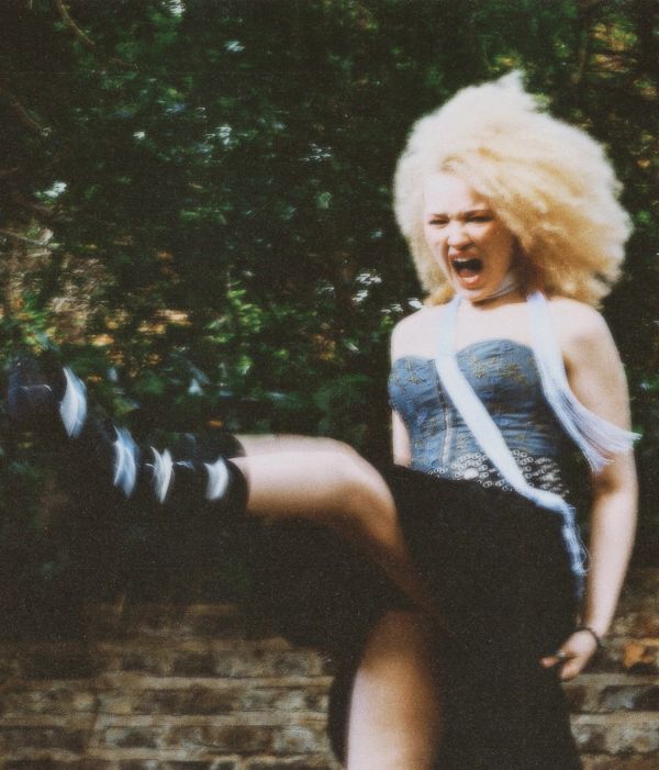 Woman with blonde curly hair shouting and kicking.