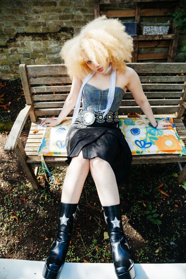 Woman with blonde afro sitting on a bench.