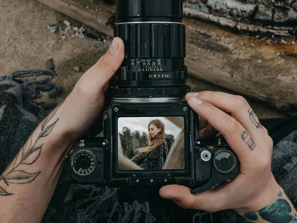 Hands holding a camera showing a photo of a smiling woman on the screen.