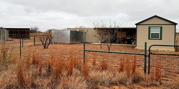 Fenced yard with small sheds and dry grass under a cloudy sky.