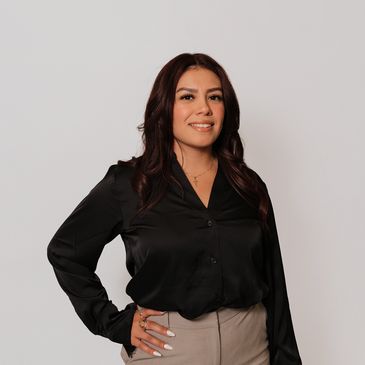 Confident woman posing in black blouse and beige pants.