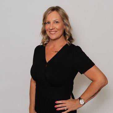 Smiling woman in a black dress posing with hand on hip.