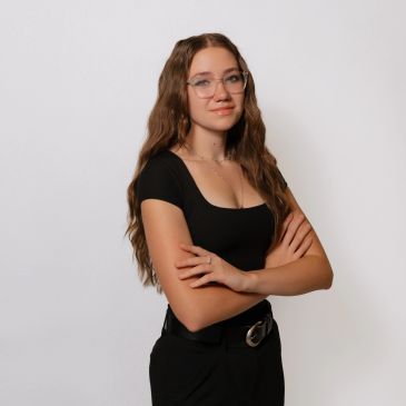 Confident young woman with glasses and long hair posing with arms crossed.