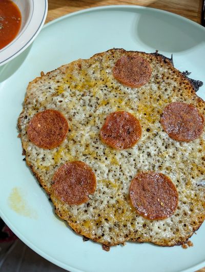 Crustless pepperoni pizza on a blue plate with melted cheese and a side of marinara sauce.