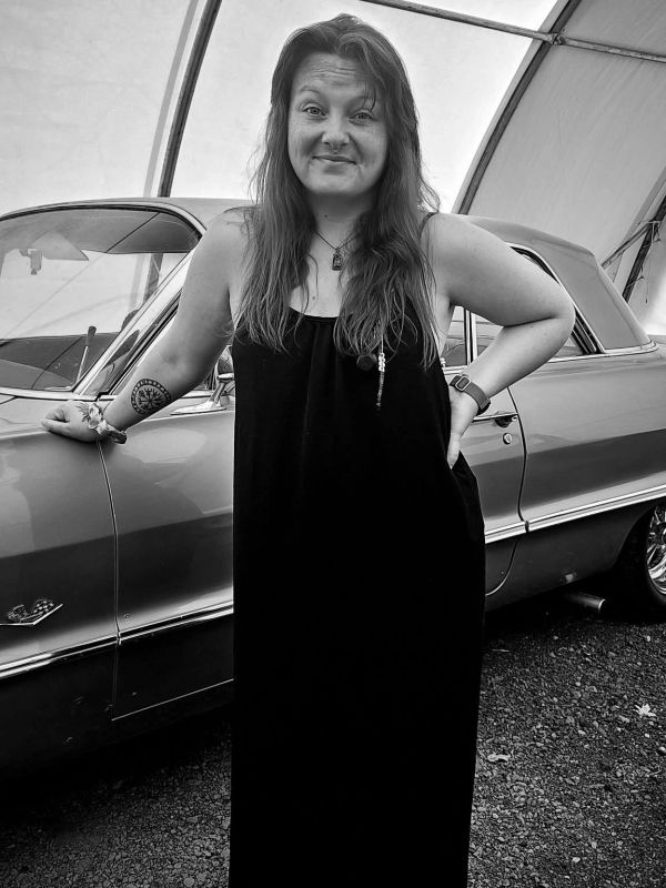 Woman in black dress posing by a classic car.