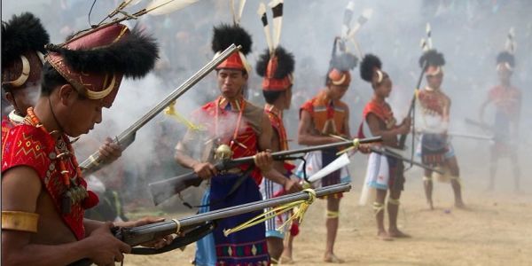 Traditional men firing rifles in a ceremonial event with smoke around.